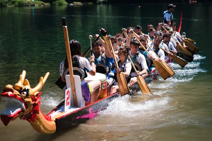 Un atleta allarga le braccia in barca, con il lago alle spalle