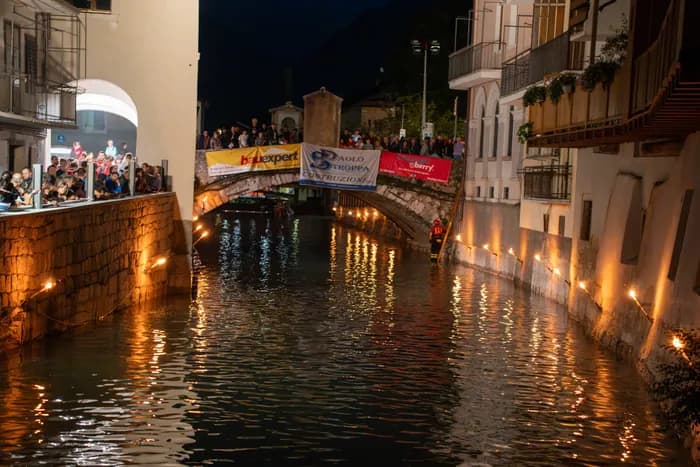Il fiume di notte, con le fiaccole accese lungo i muri e il pubblico sul ponte