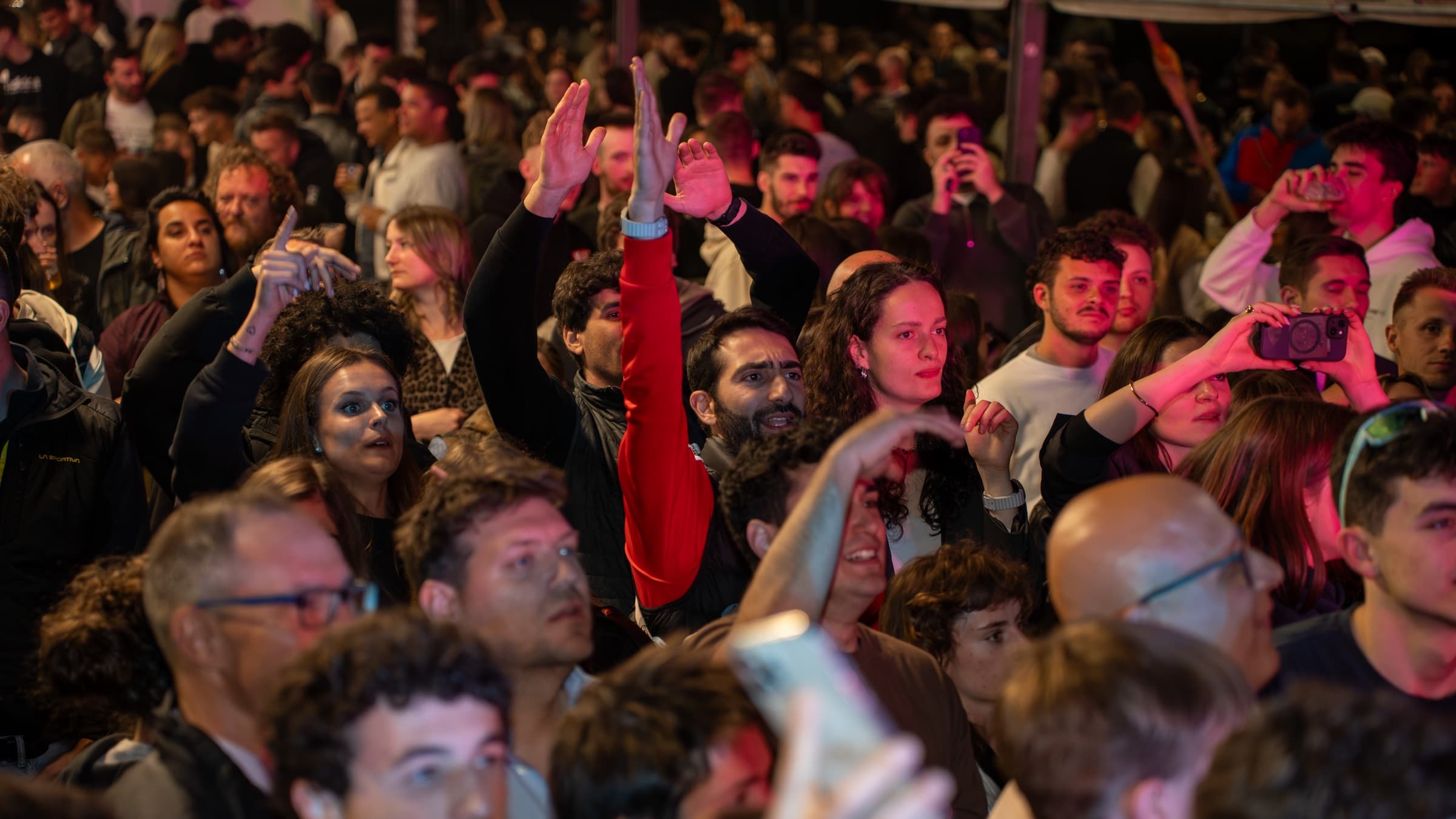 Folla con mani gonfiabili alzate durante la Sagra di Serso 2026, tra palme e luci notturne