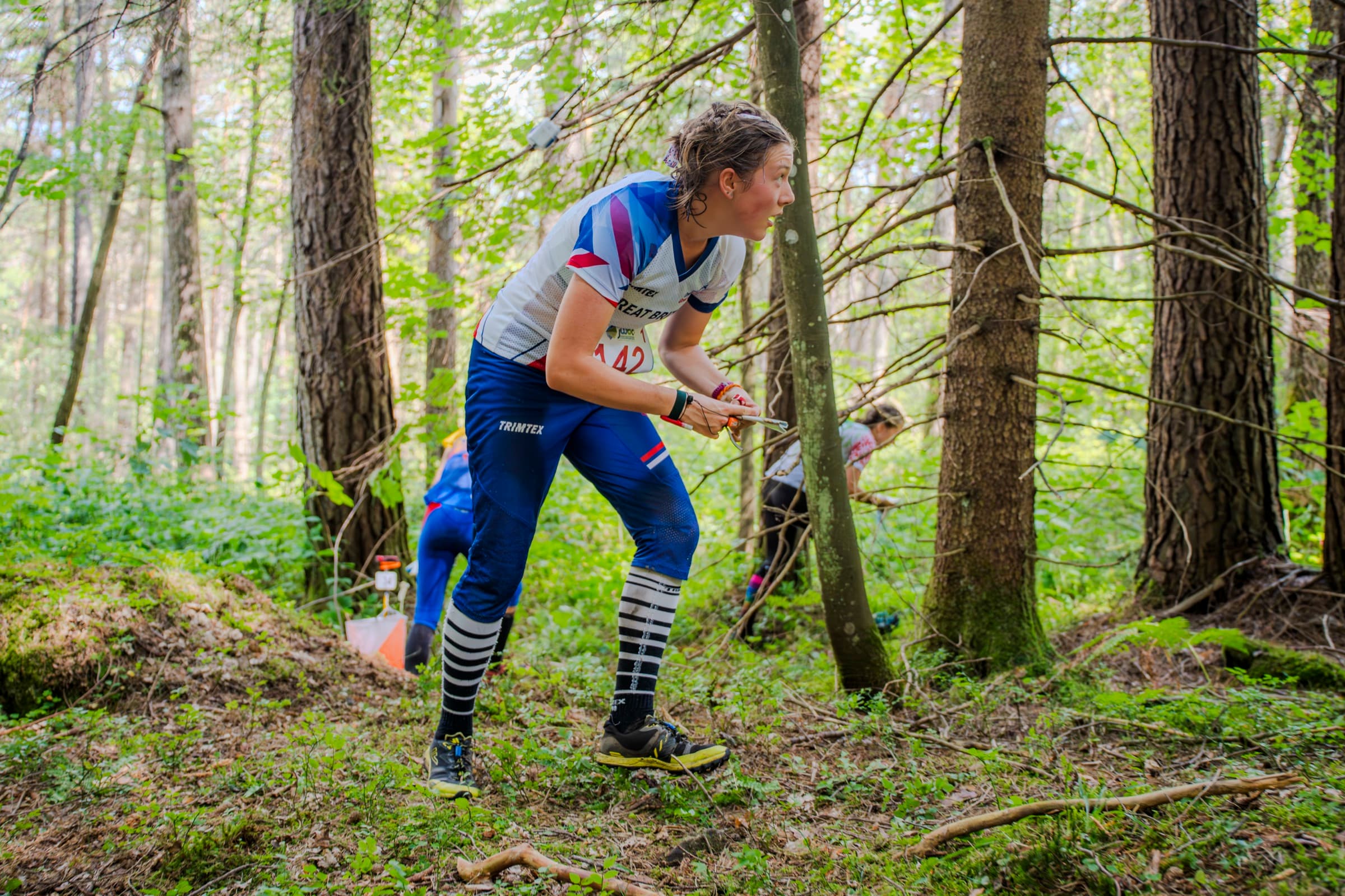 Atleta di orienteering china in avanti tra gli alberi, alla ricerca della prossima lanterna
