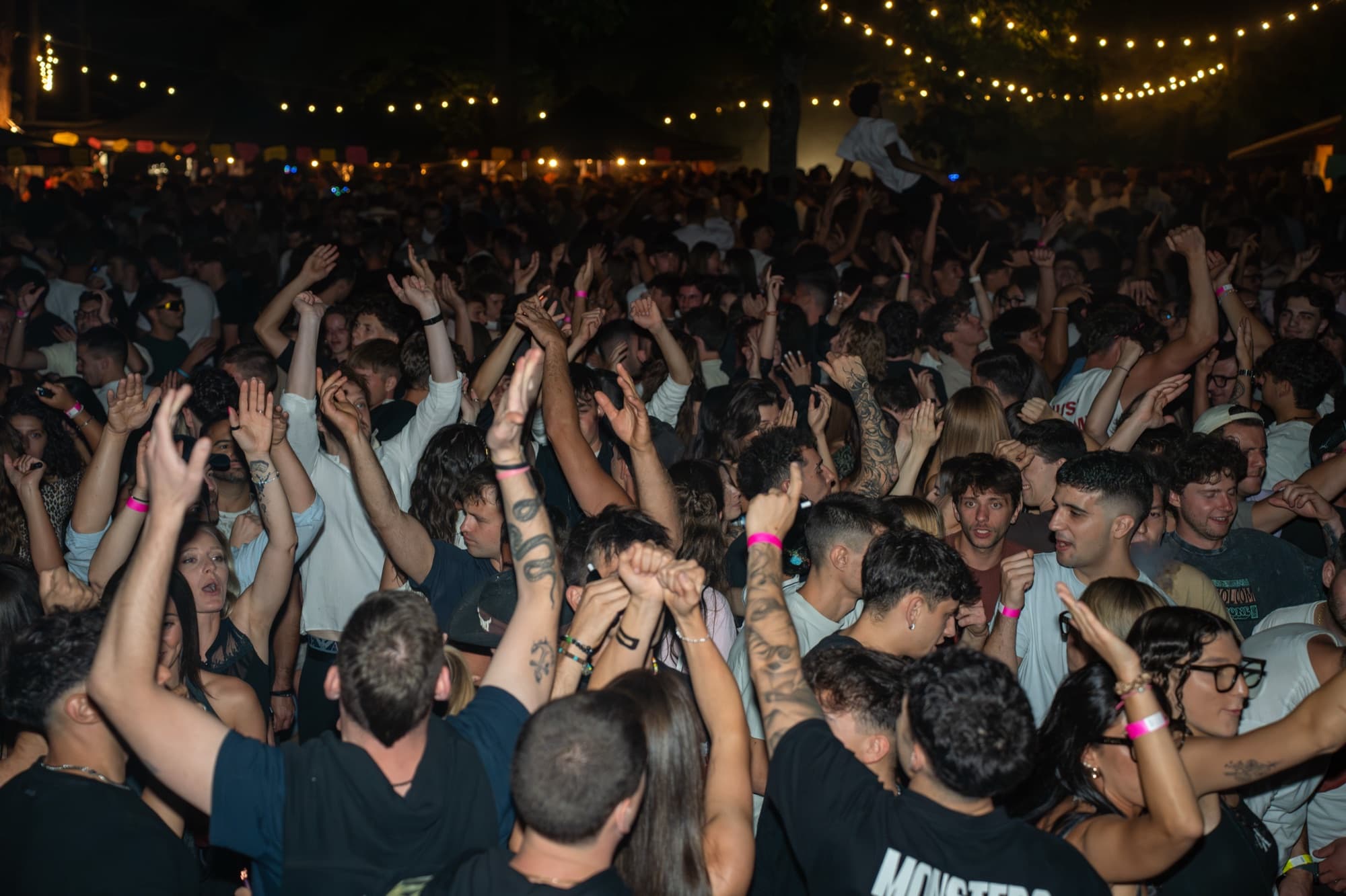 La folla di un festival notturno balla con le mani alzate sotto le luci a festone