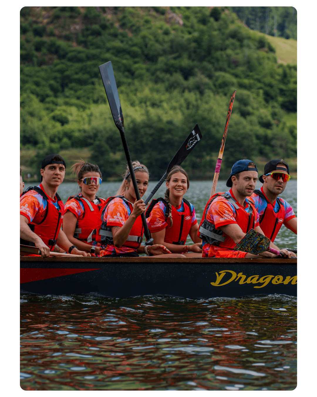 Equipaggio con i giubbotti di salvataggio arancioni a bordo del dragon boat, pale alzate