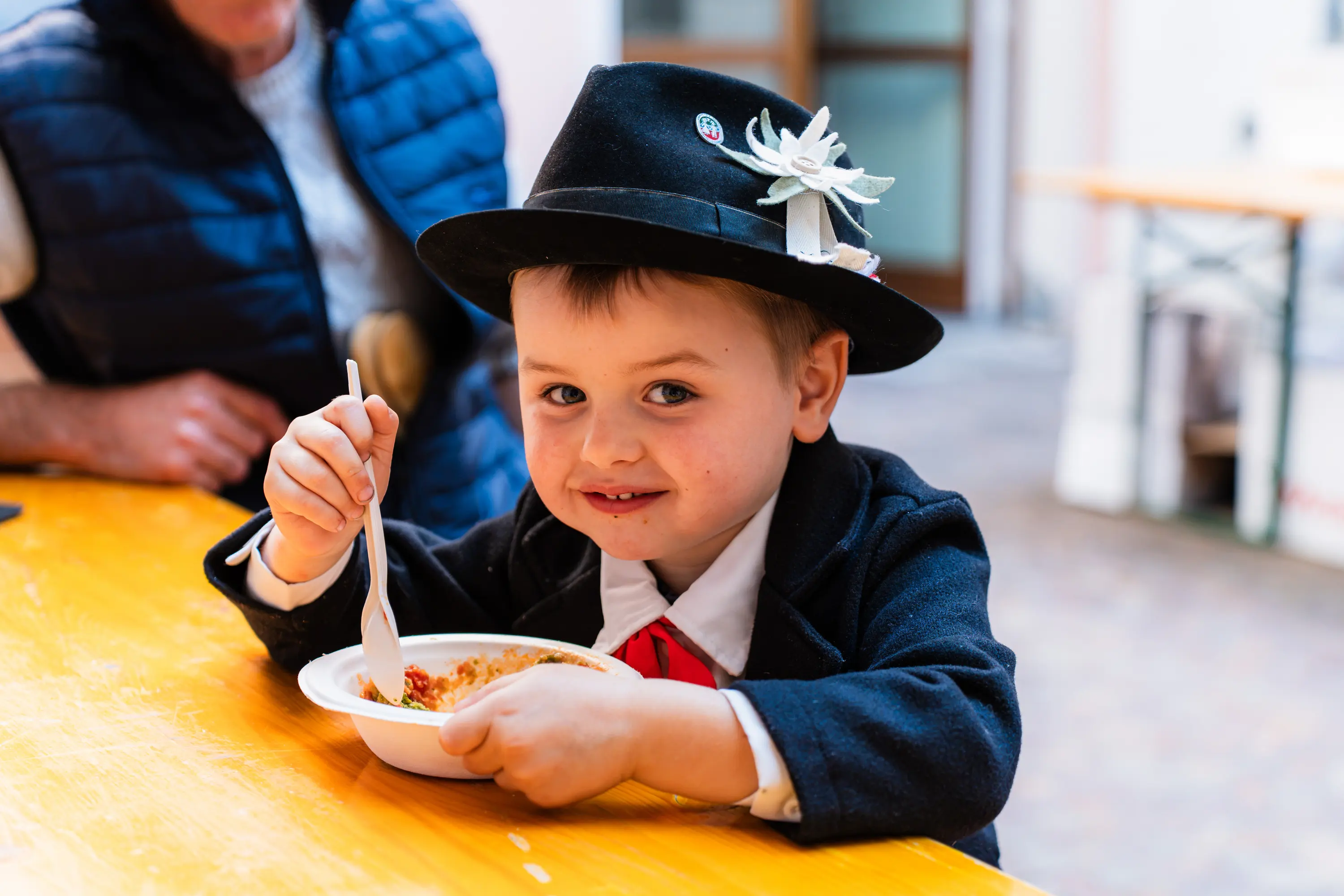 Un bambino con il cappello tradizionale mangia il suo canederlo alla tavolata