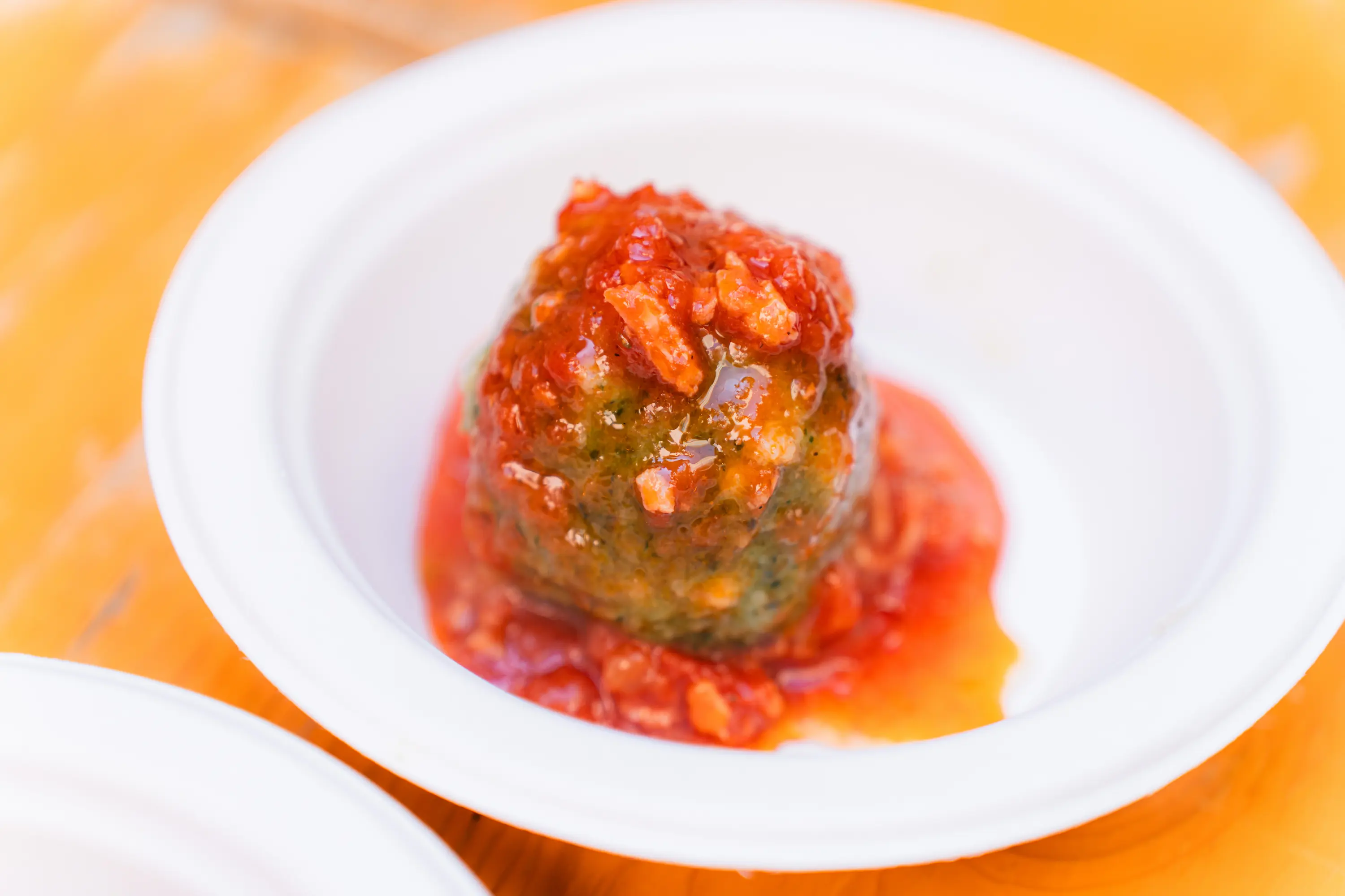 Un canederlo agli spinaci con il sugo di pomodoro, in un piatto di carta