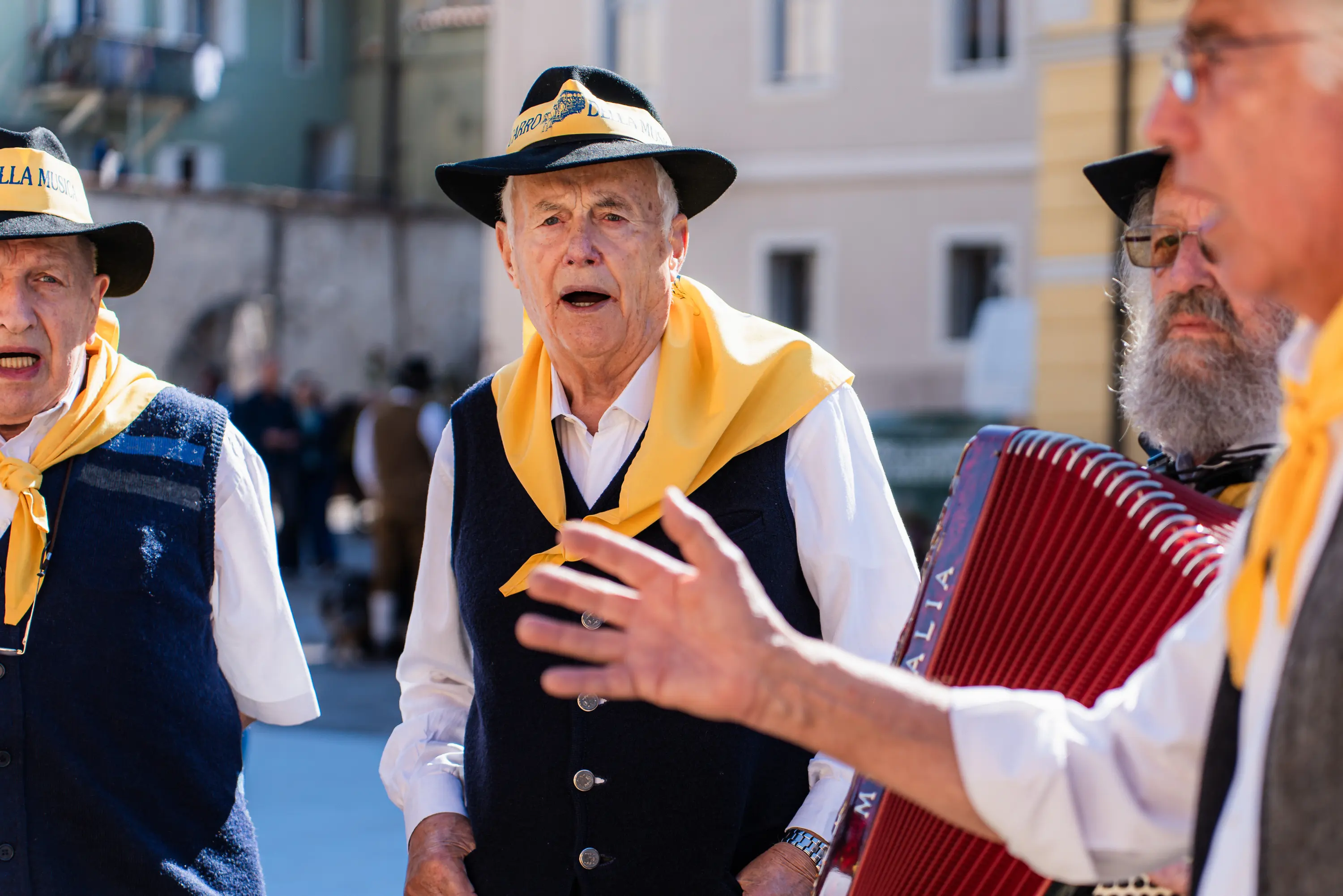 Tre uomini con il fazzoletto giallo al collo cantano accompagnati dalla fisarmonica