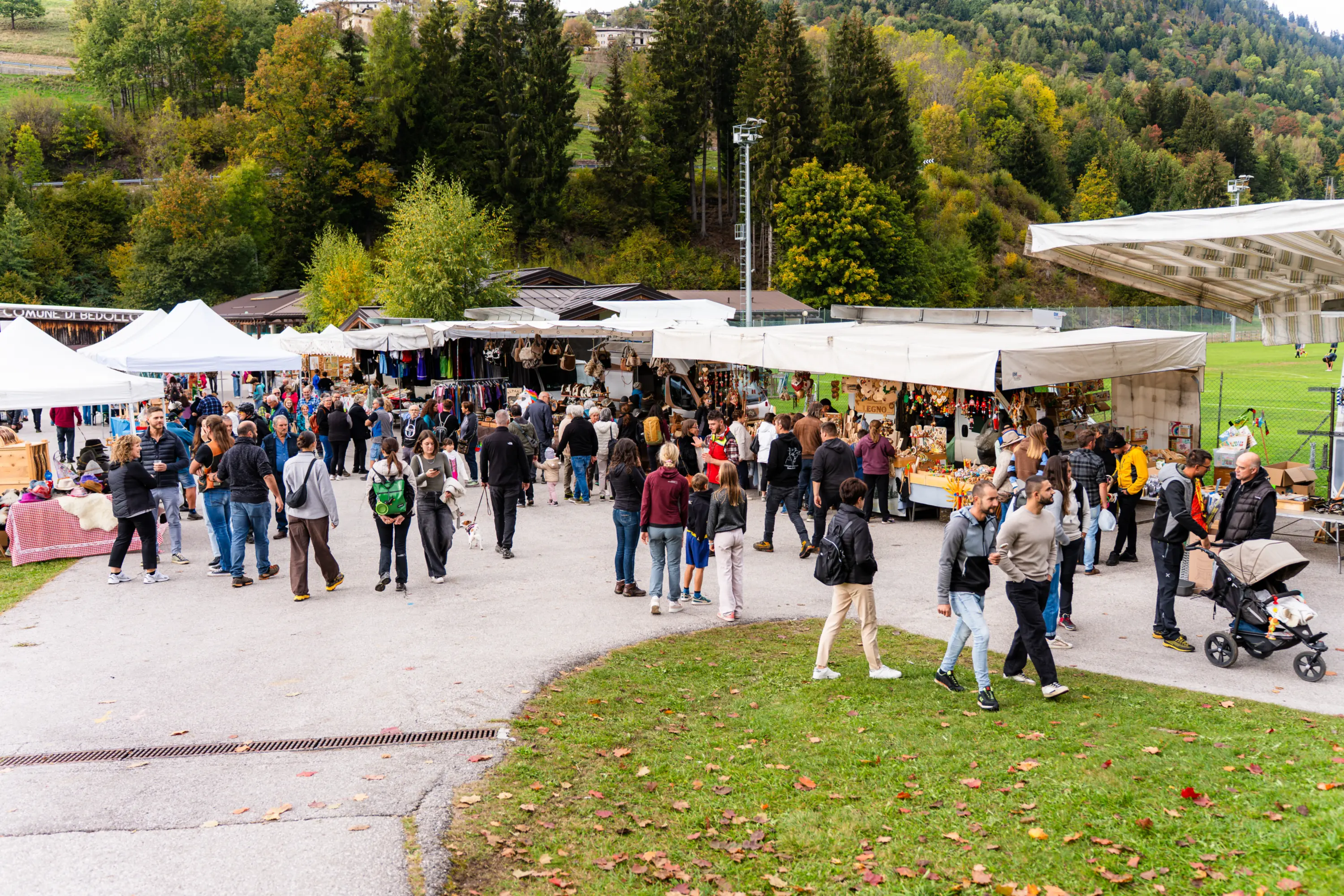 Il viale delle bancarelle sotto i gazebo bianchi, pieno di gente, con il bosco alle spalle