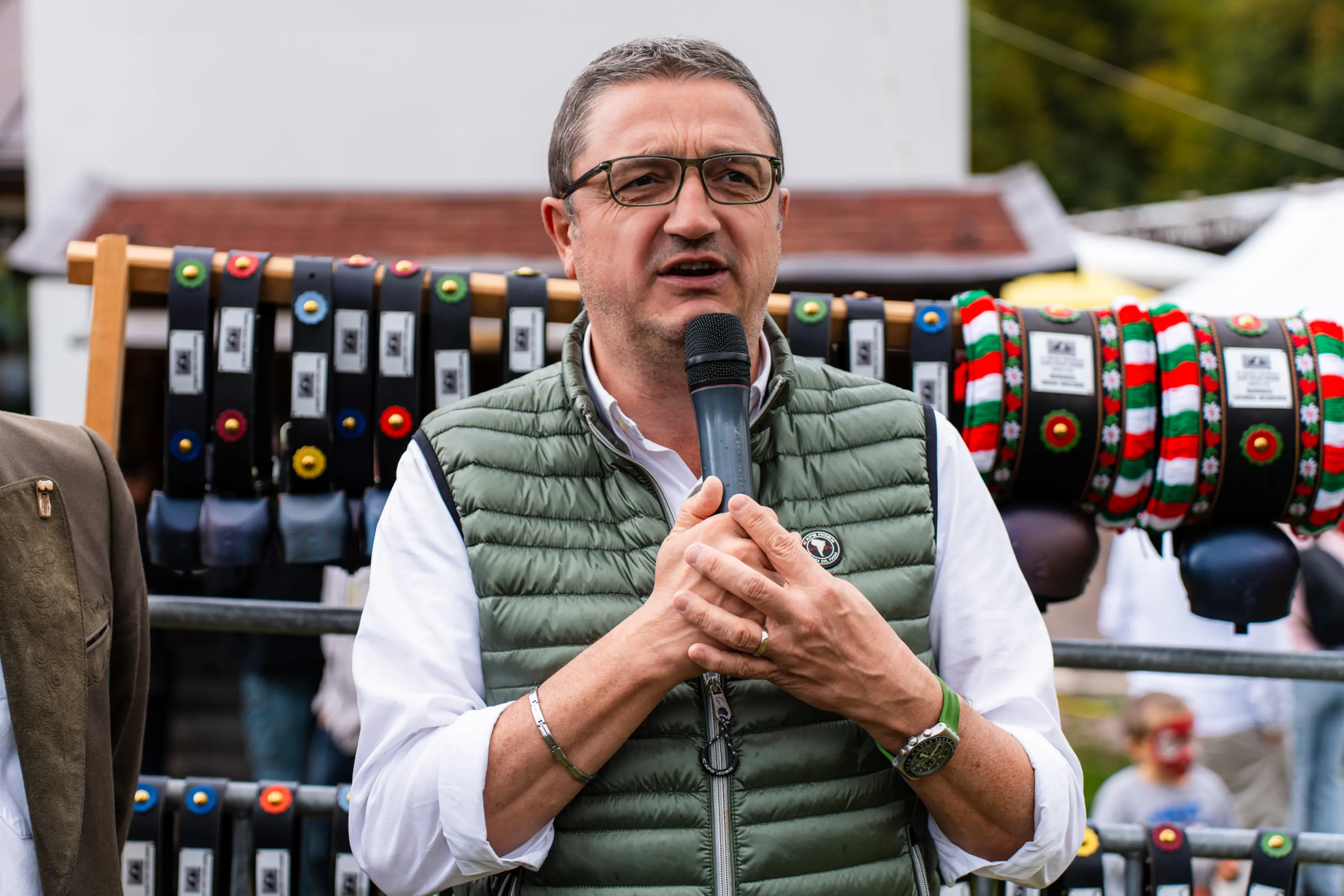 Un uomo con il gilet verde parla al microfono davanti ai collari appesi