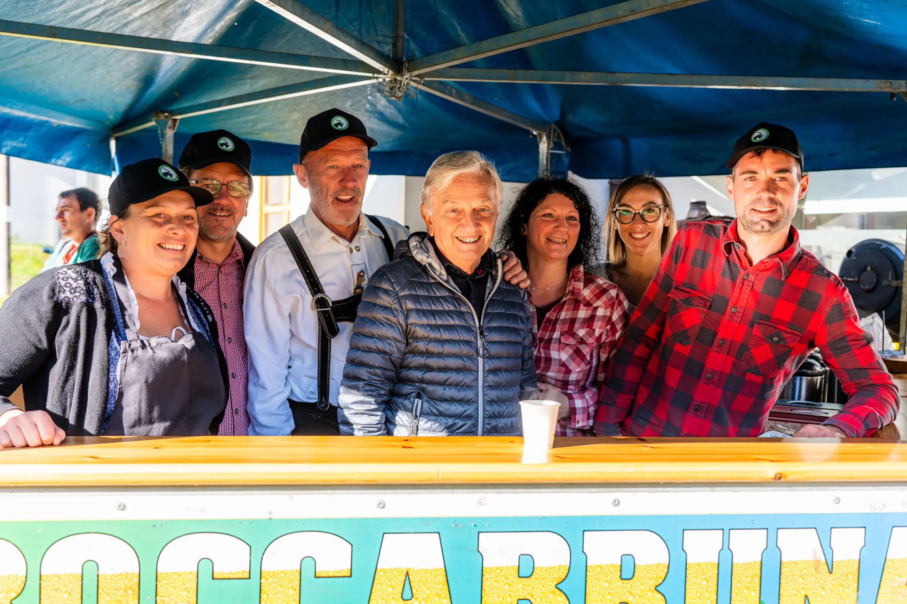 La squadra di uno stand sorride dietro il banco, sotto il gazebo blu