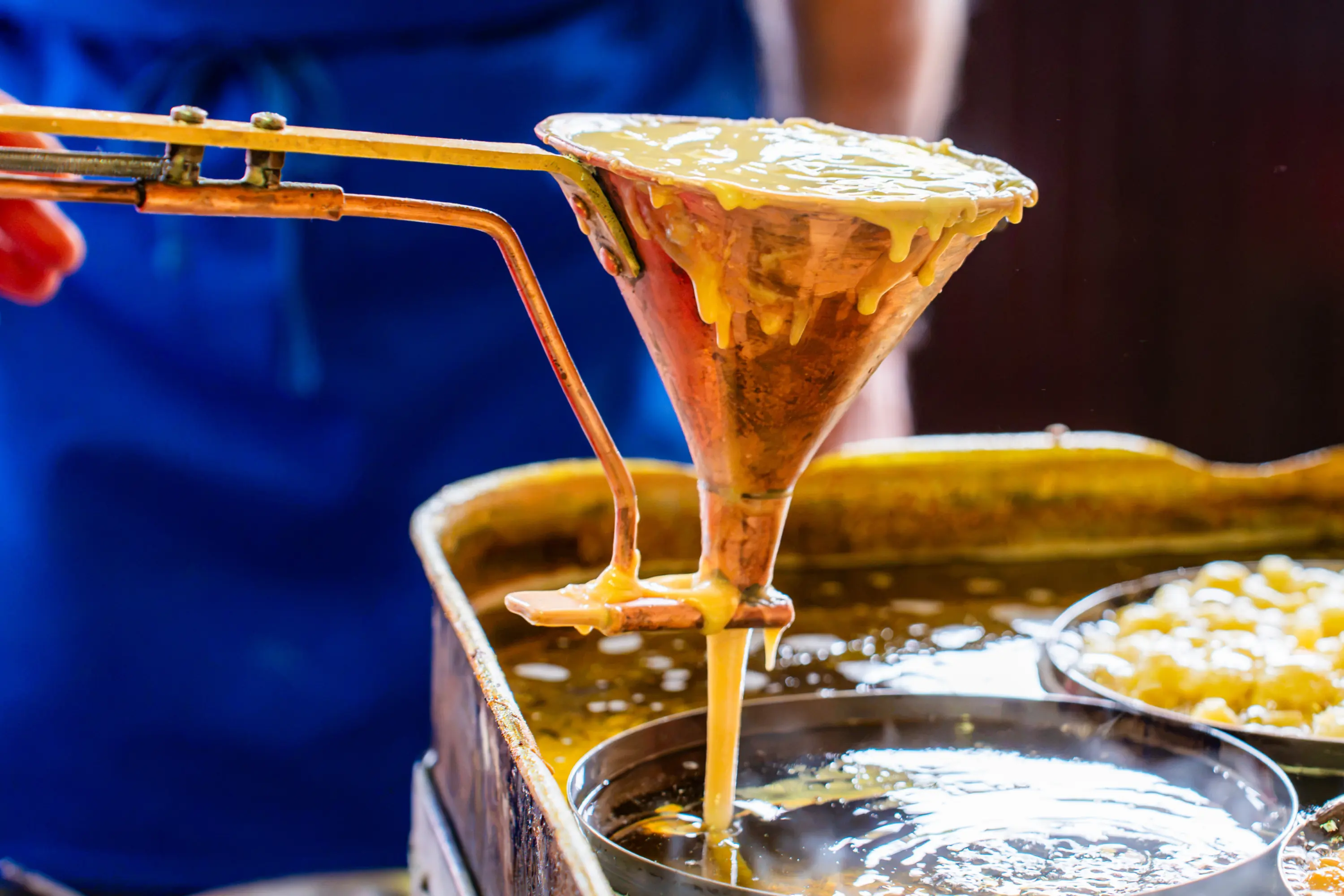 La pastella degli strauben cola dall'imbuto di rame nell'olio