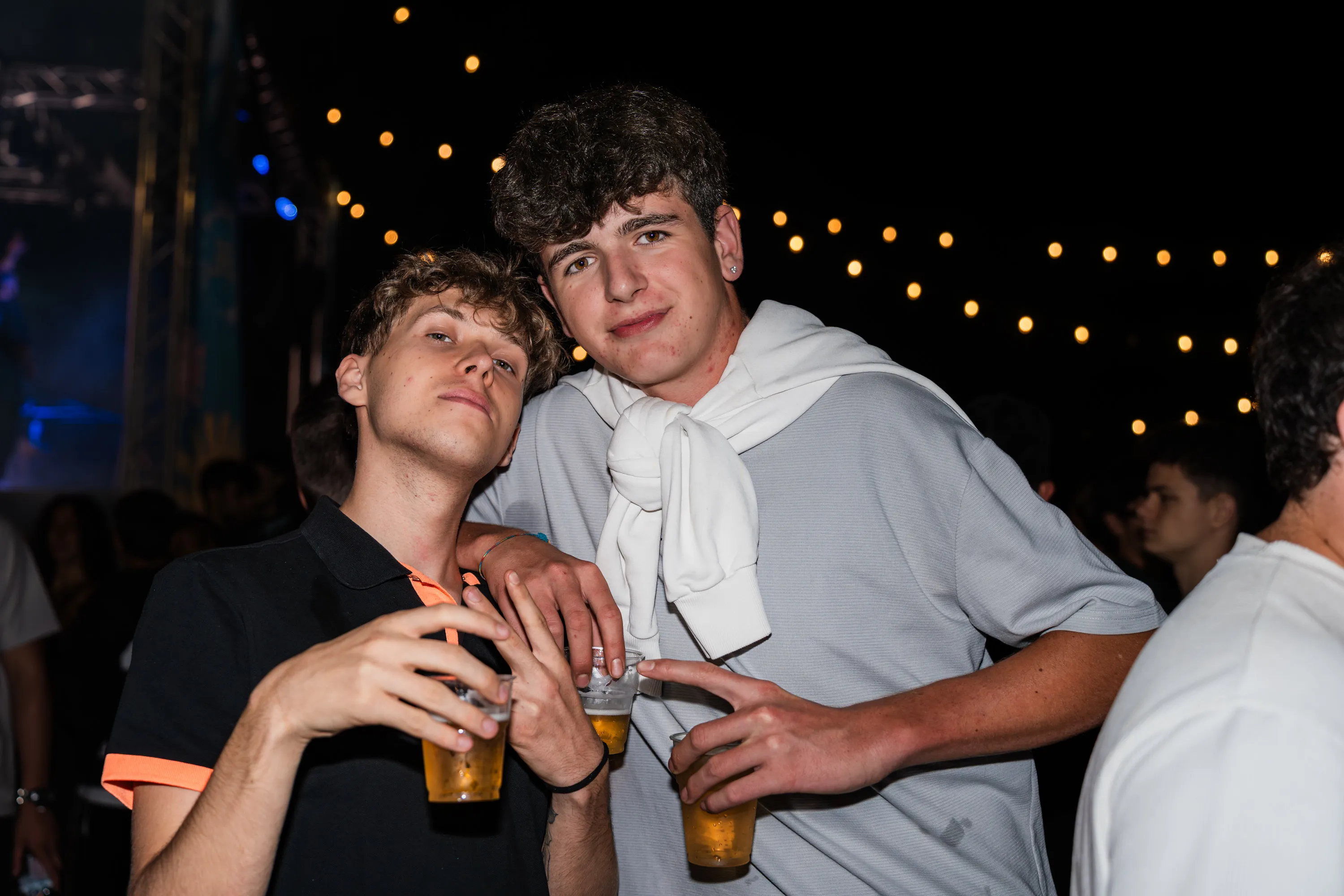 Due ragazzi con i bicchieri di birra sotto le lucine della festa