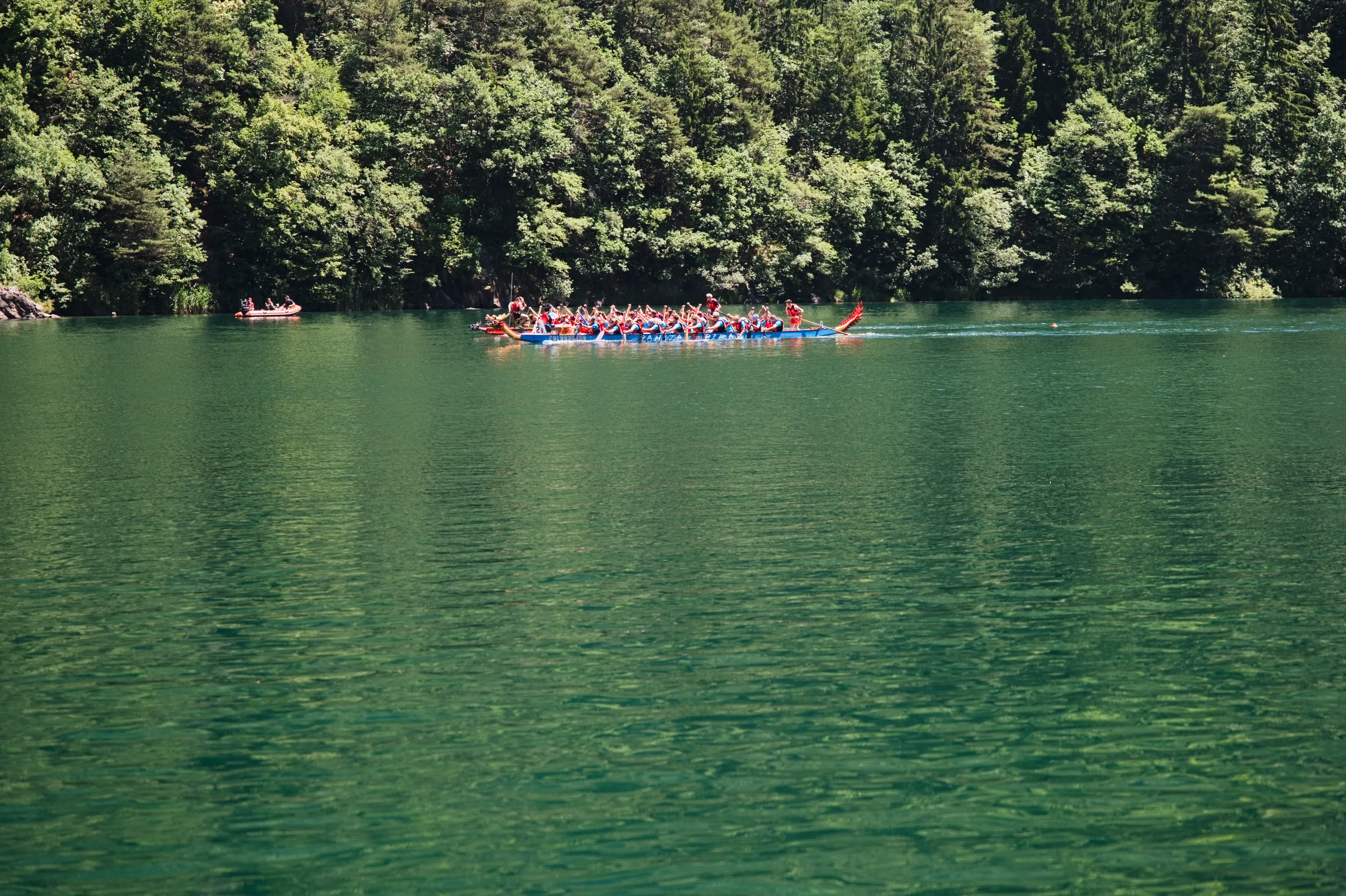 Una barca drago attraversa il lago vista dall'altra riva, piccola dentro il bosco