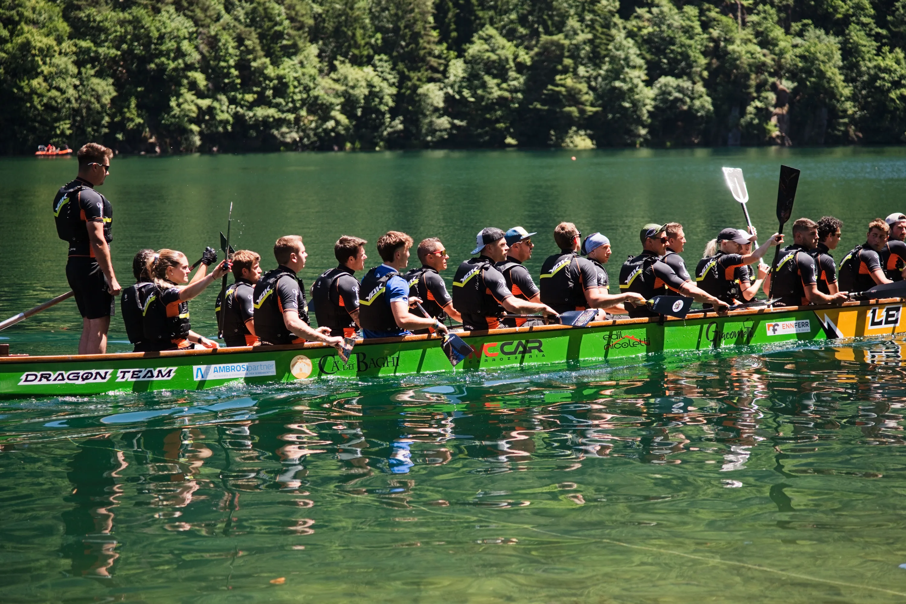 Una barca drago verde attraversa il lago delle Lases, chiuso dal bosco sulle rive
