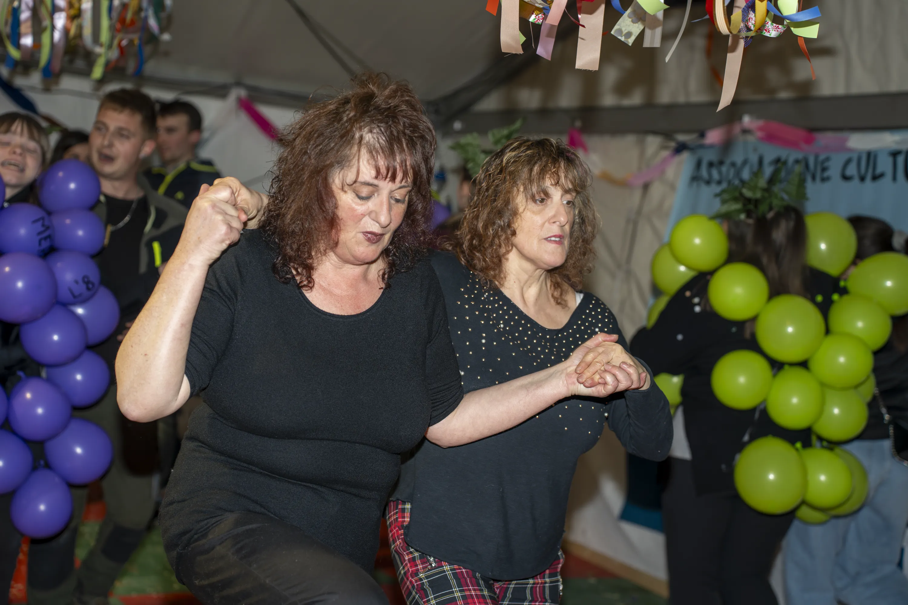 Due donne in abiti normali ballano in mezzo ai costumi a grappolo d'uva