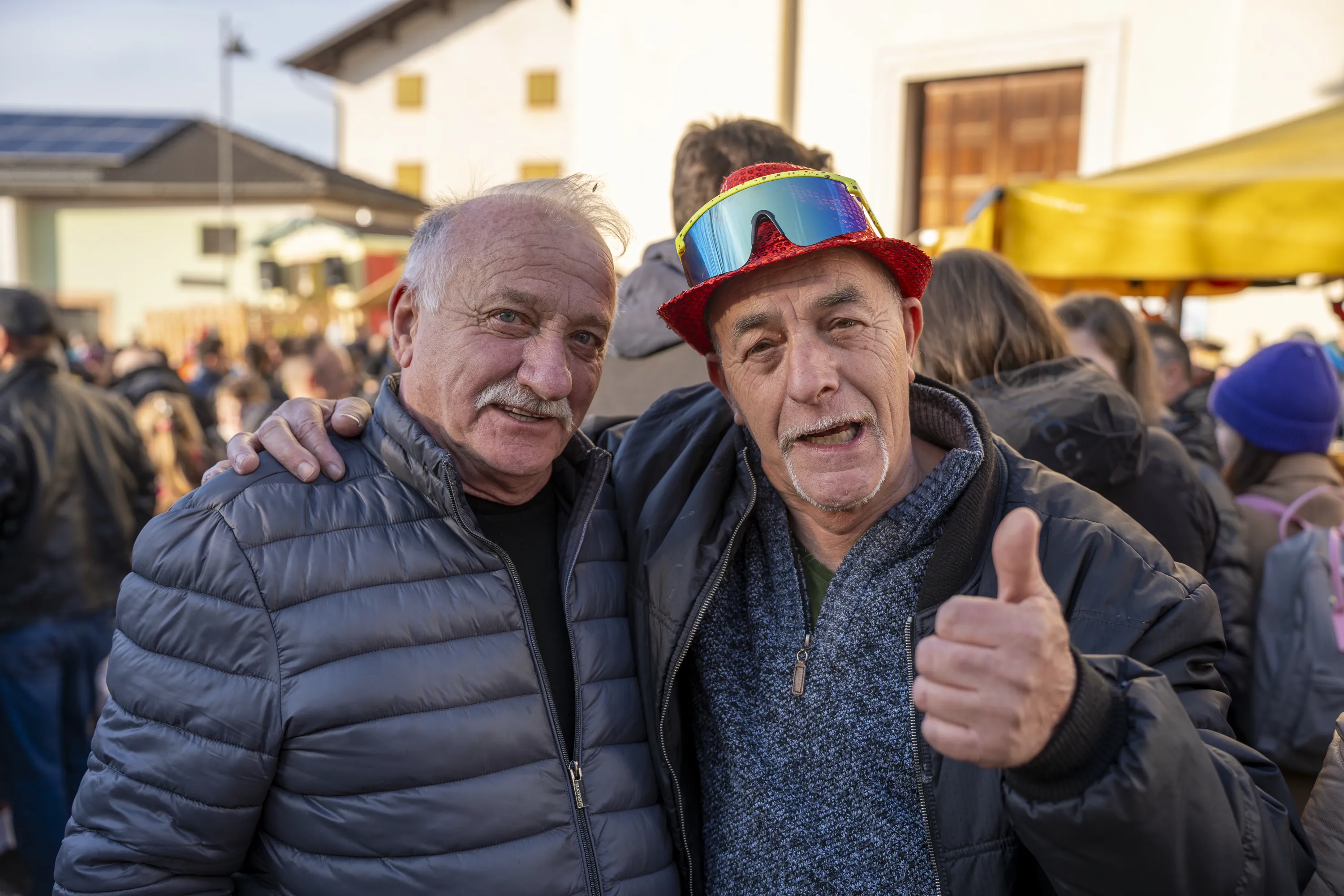 Due uomini anziani, uno con il cappello arcobaleno, alzano il pollice
