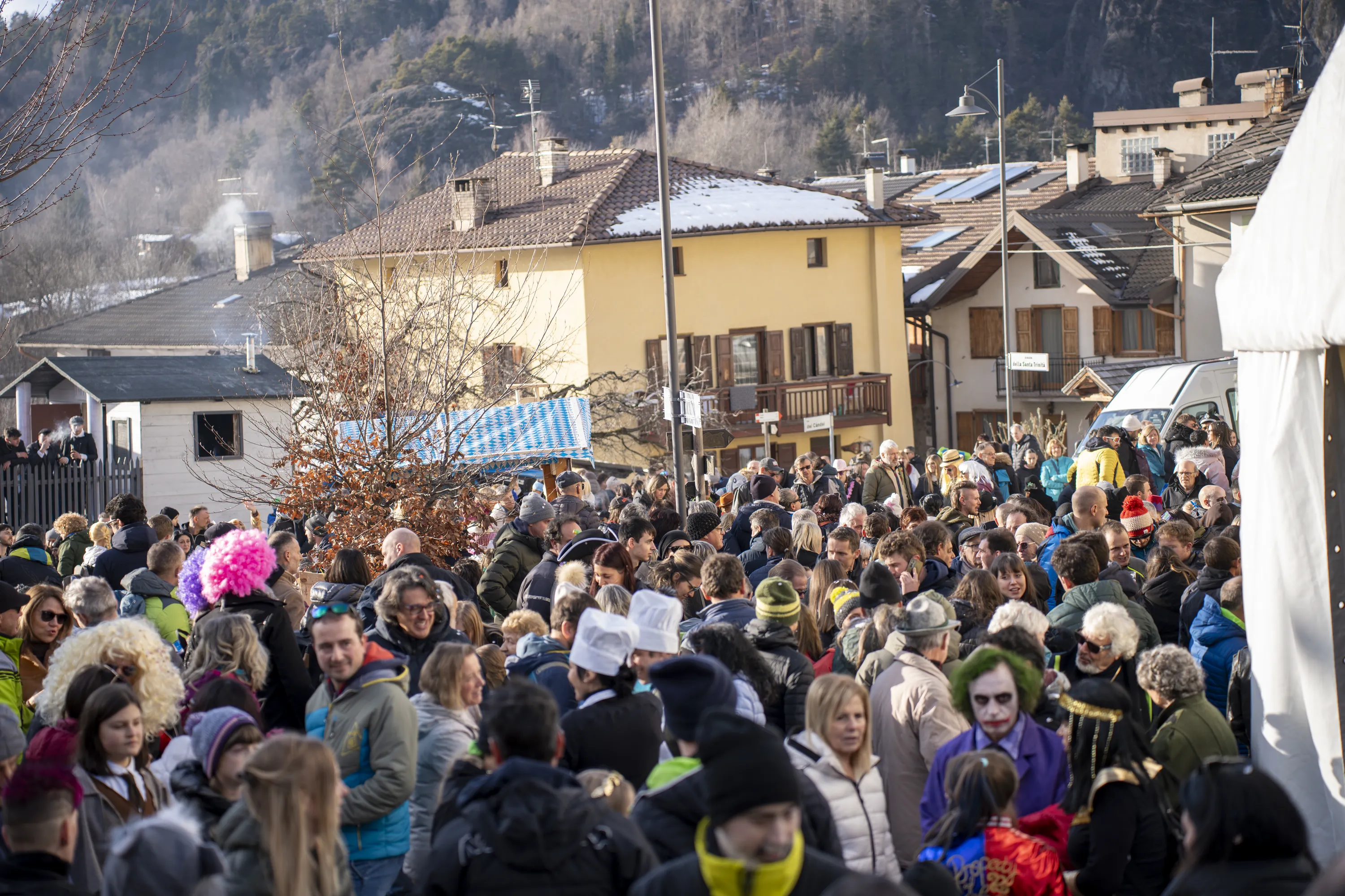 La via principale di Faida di Piné piena di gente in maschera, vista dall'alto, con le case e la montagna alle spalle