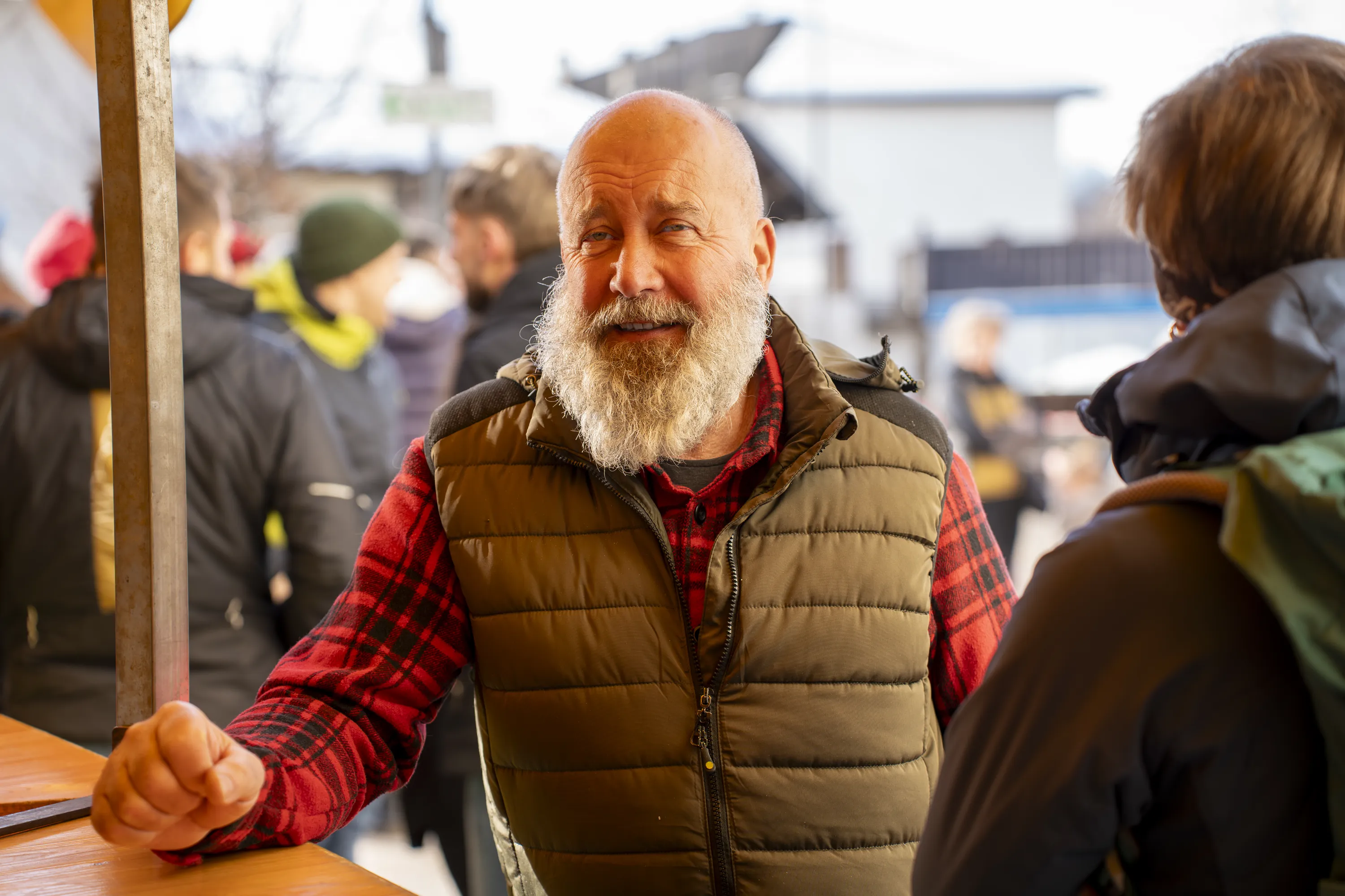 Un uomo con la barba bianca e il gilet rosso sorride in mezzo alla folla