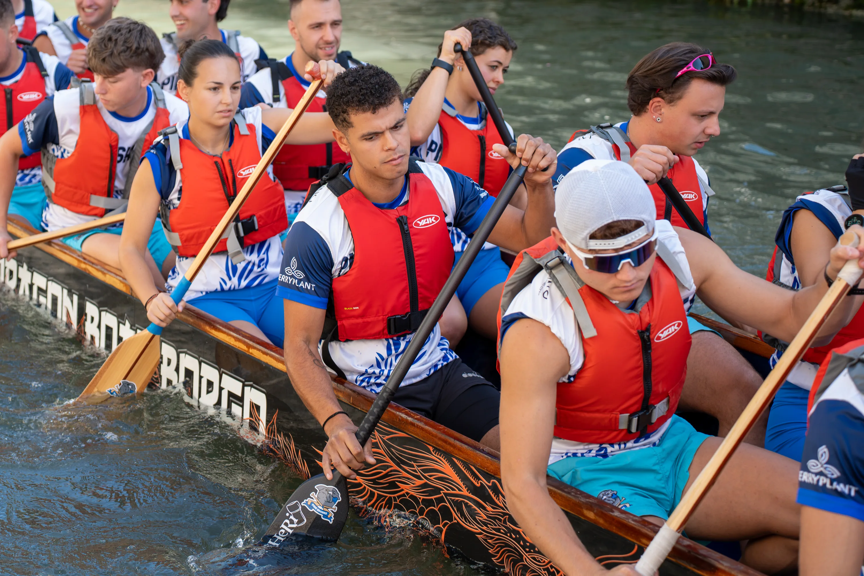 Un equipaggio in giubbotto rosso visto da vicino, con le pagaie in acqua accanto alla scritta Dragon Boat Borgo
