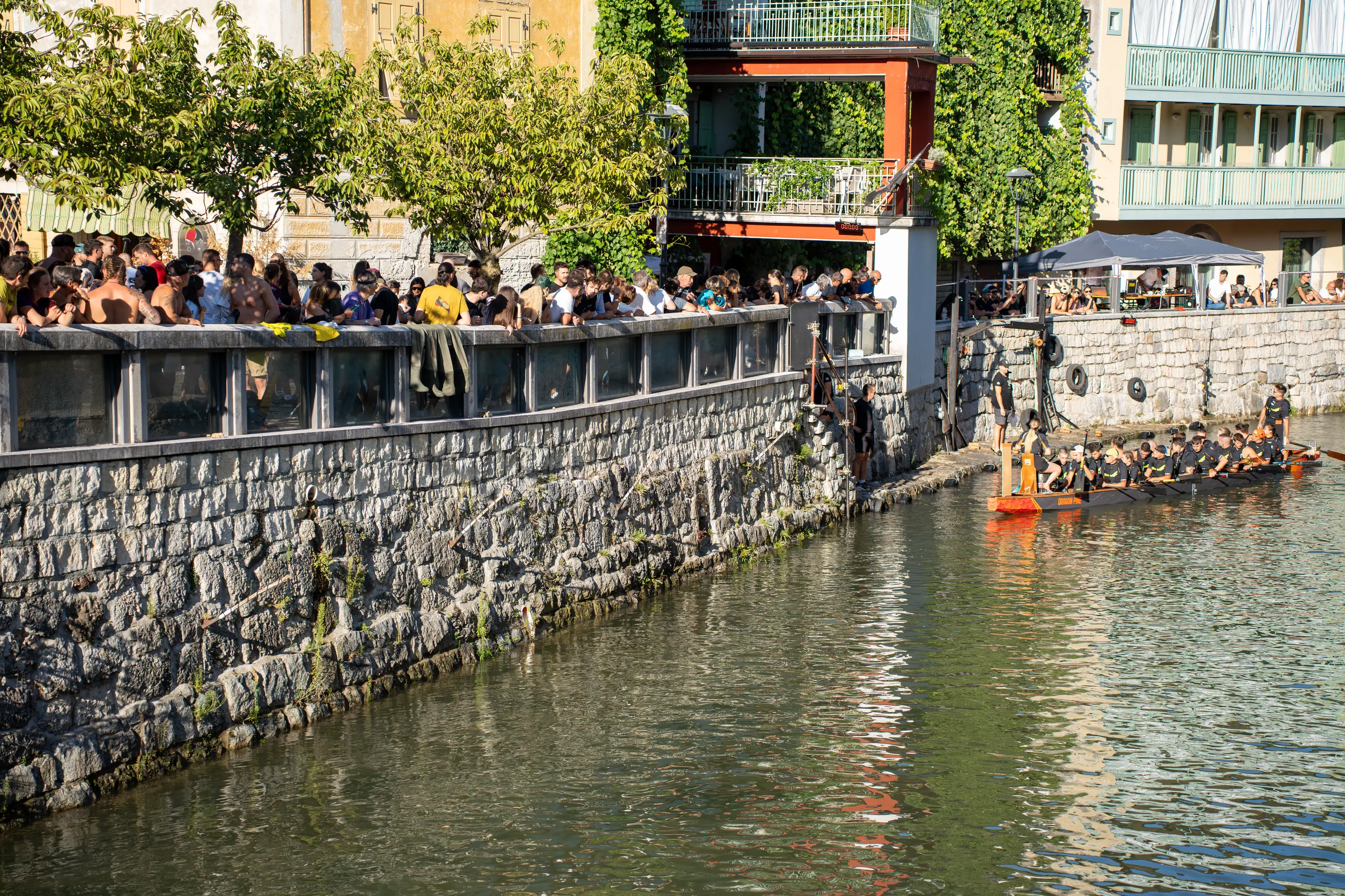 Il pubblico affacciato al parapetto sopra il muro di pietra del Brenta, con una barca in acqua sotto la riva