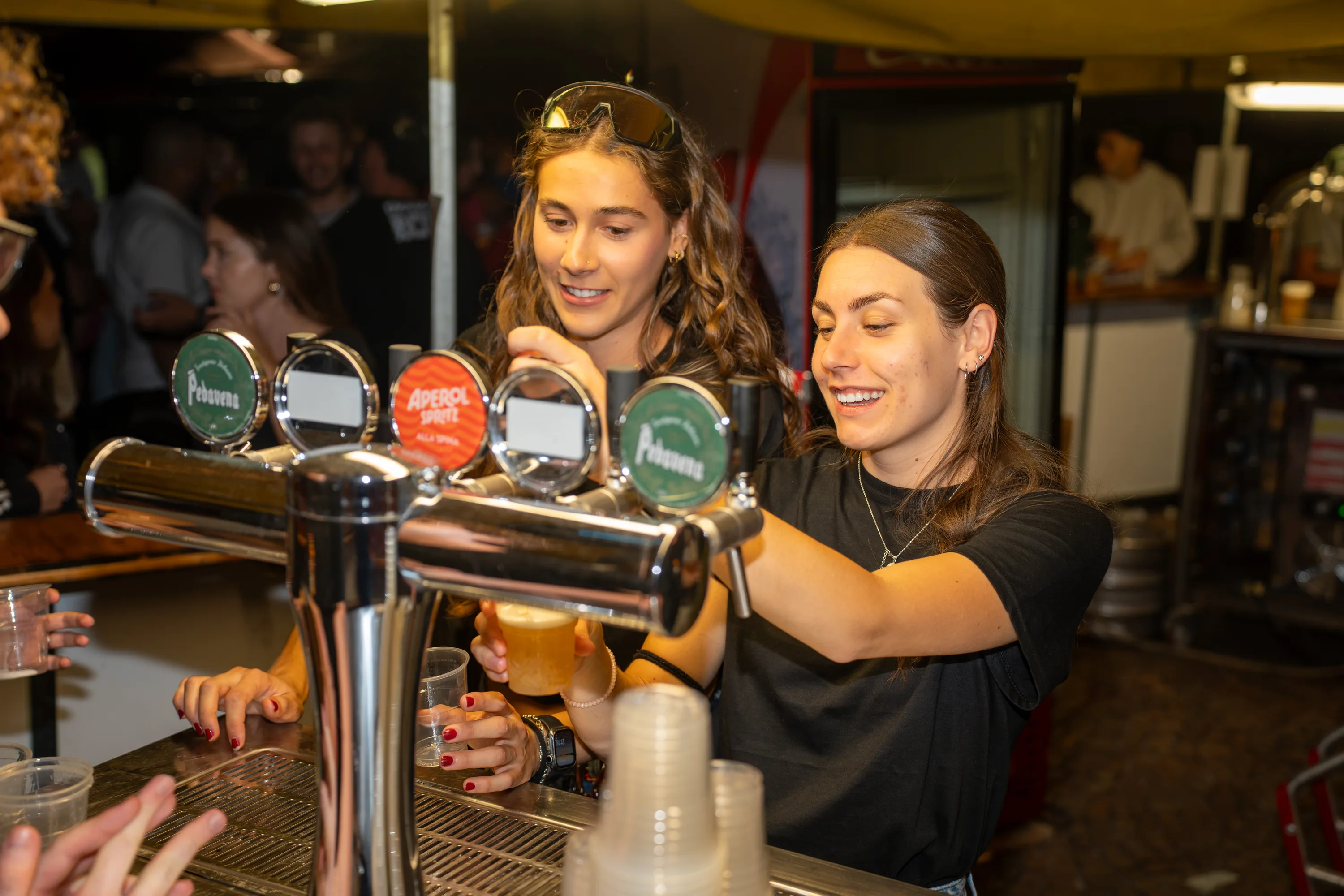 Due ragazze spillano la birra al banco della festa