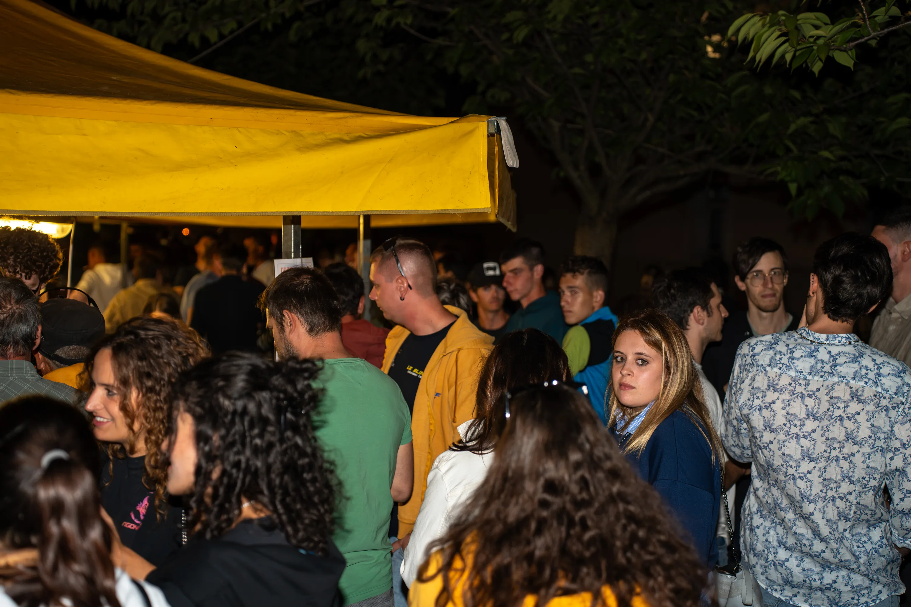 La folla della festa sotto i tendoni gialli, di sera