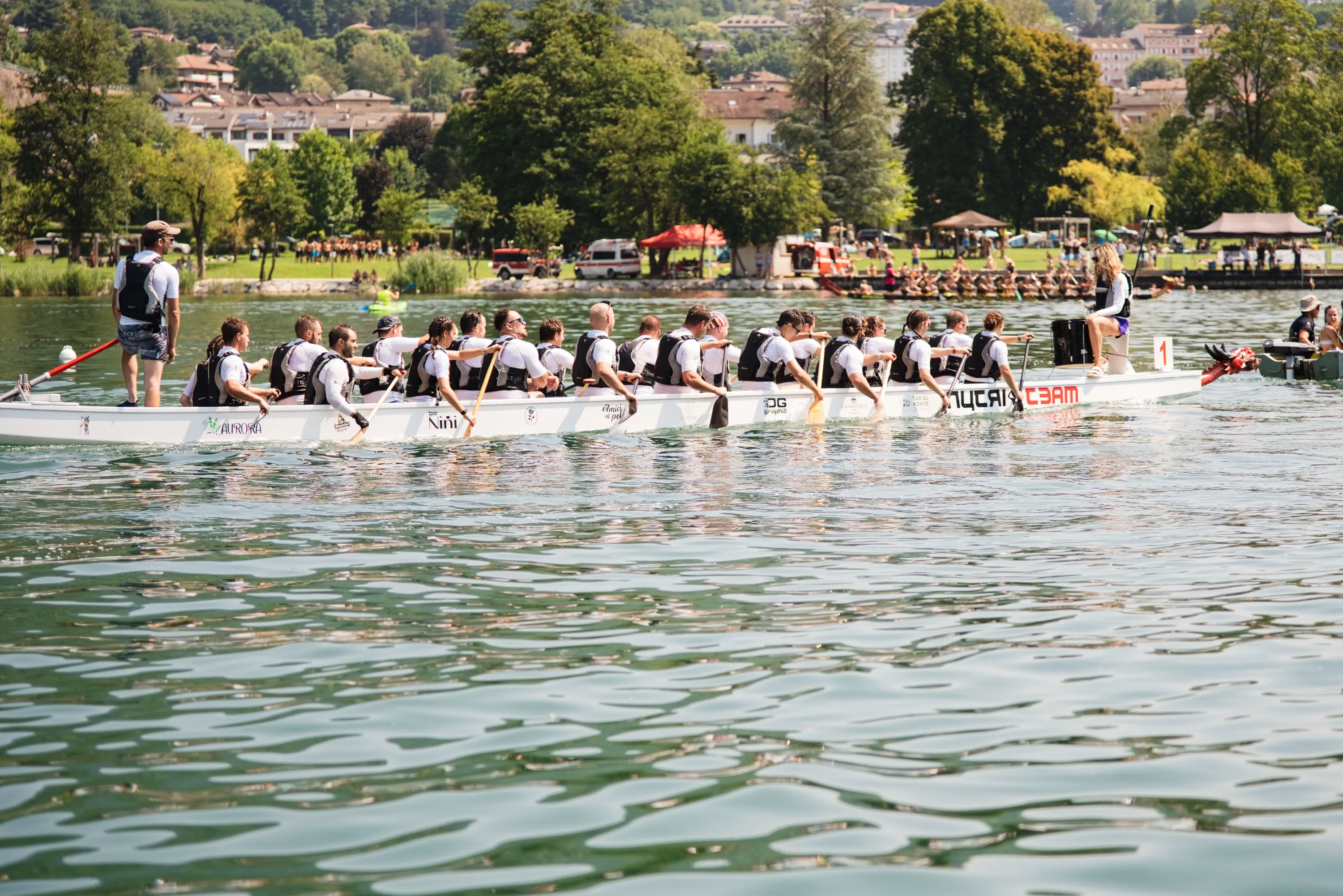 Una barca drago in gara sul lago di Levico, con il paese e le montagne alle spalle