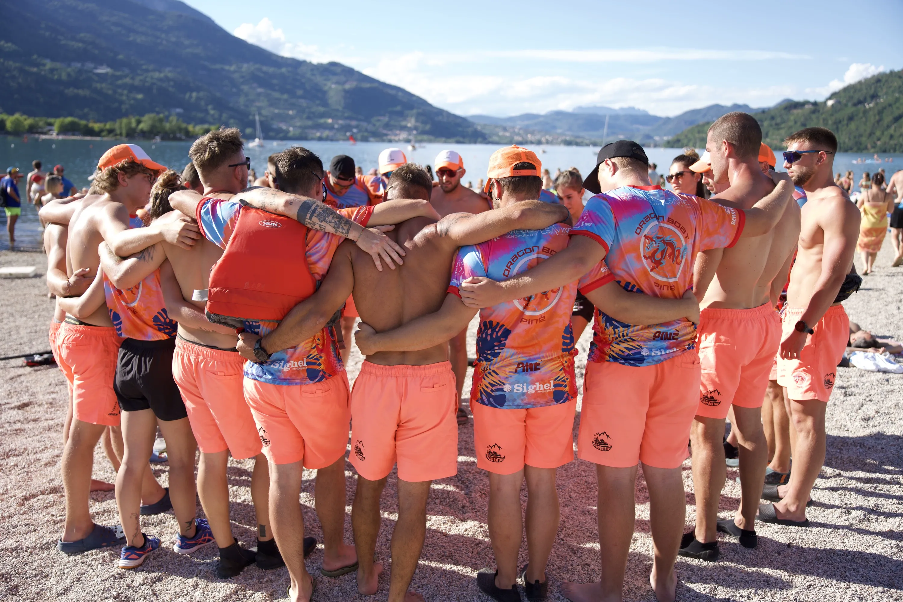 Una squadra in maglia arancione riunita in cerchio sulla riva
