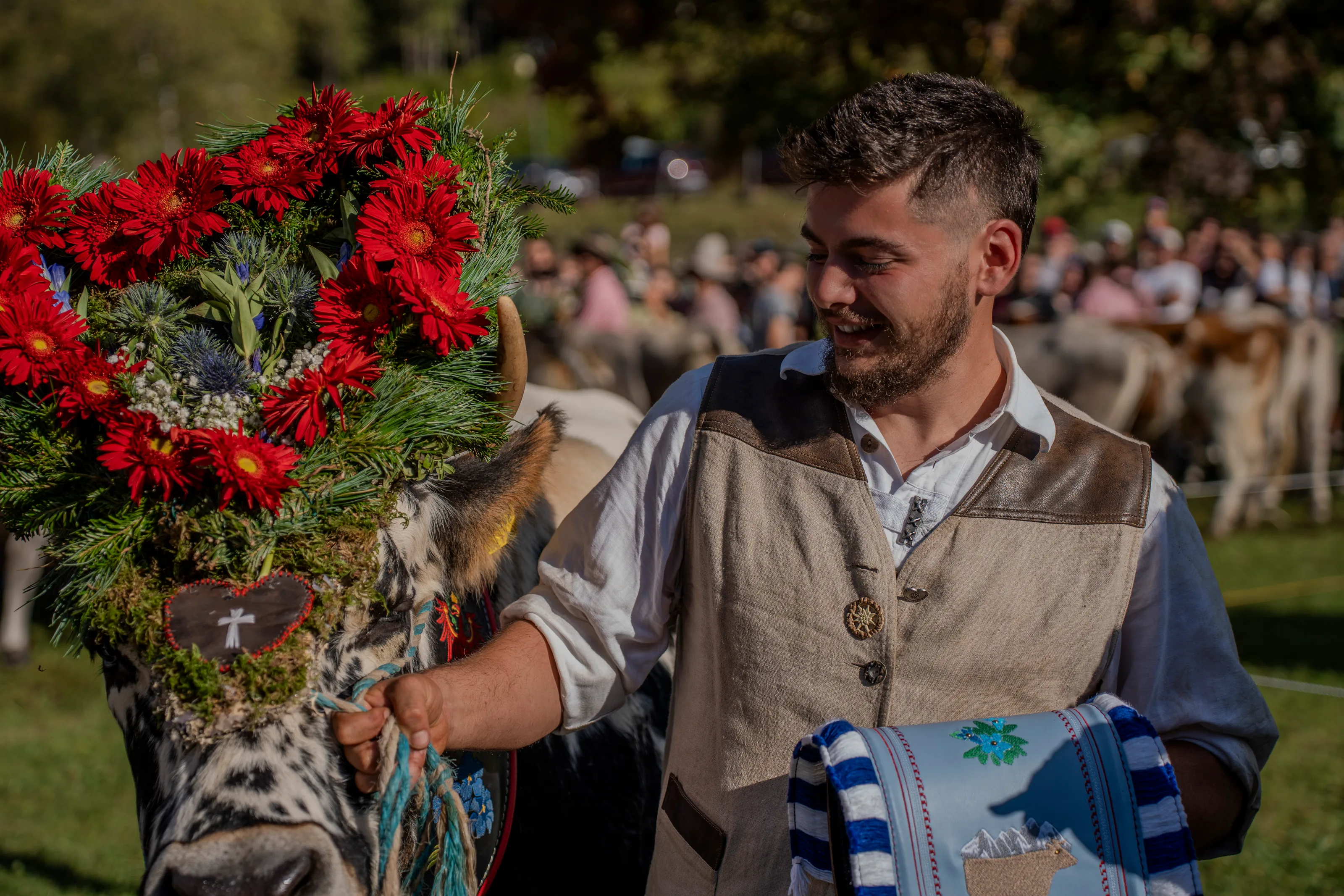 Un uomo in abito tradizionale sorride accanto alla mucca con la corona a forma di cuore