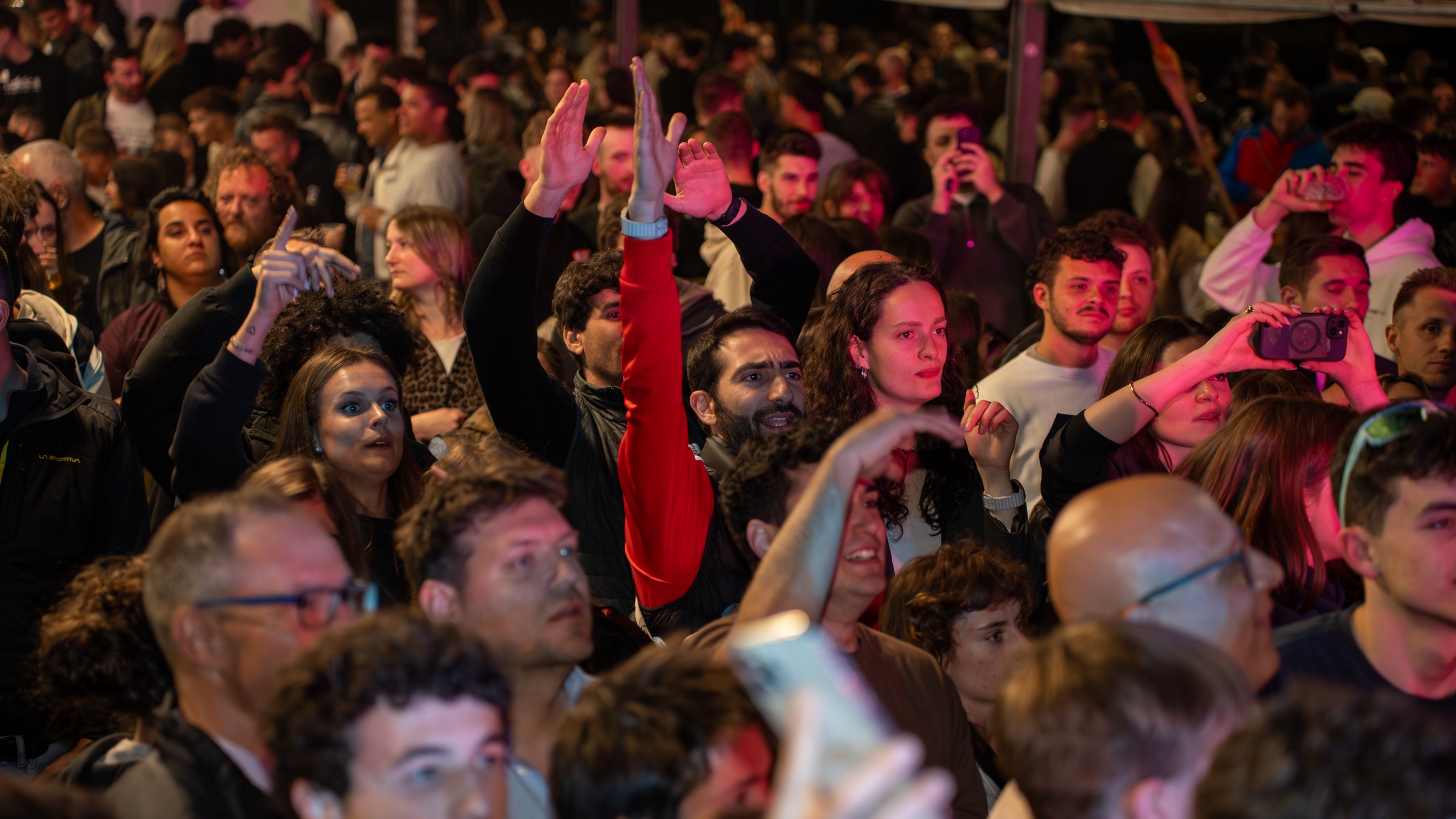 Folla con mani gonfiabili alzate durante la Sagra di Serso 2026, tra palme e luci notturne