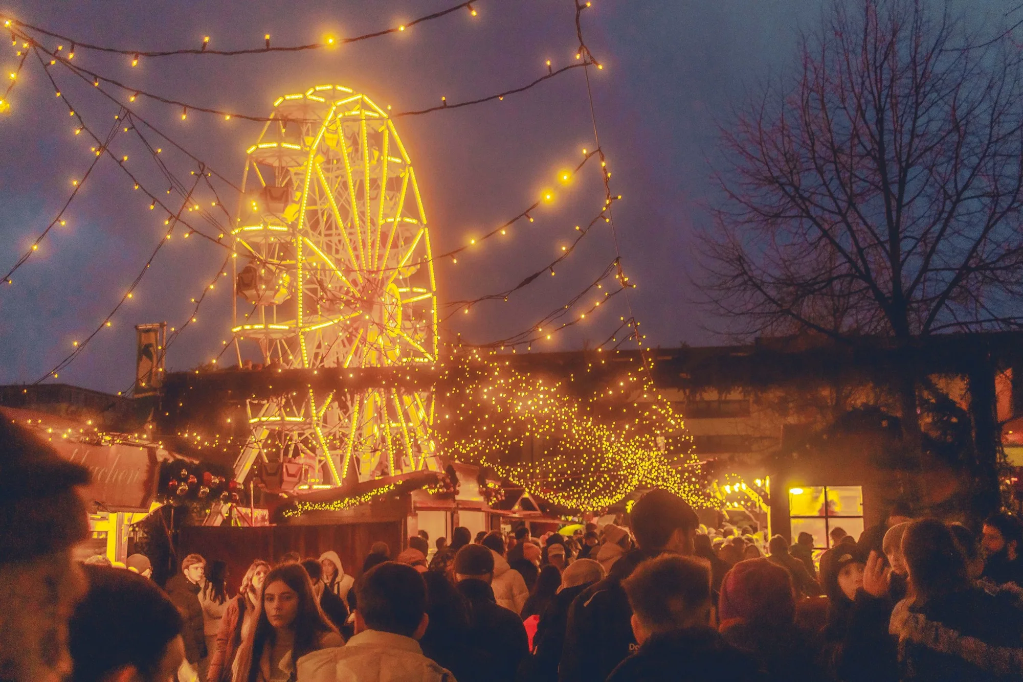 Un mercatino di Natale di sera, con la ruota panoramica illuminata sopra la folla
