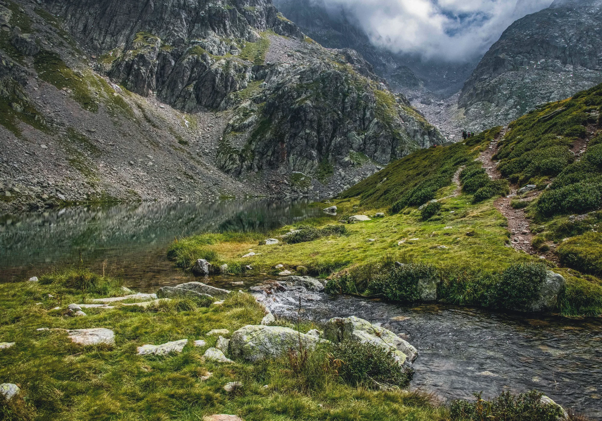Un paesaggio di montagna con il verde, un lago alpino calmo e un ruscello