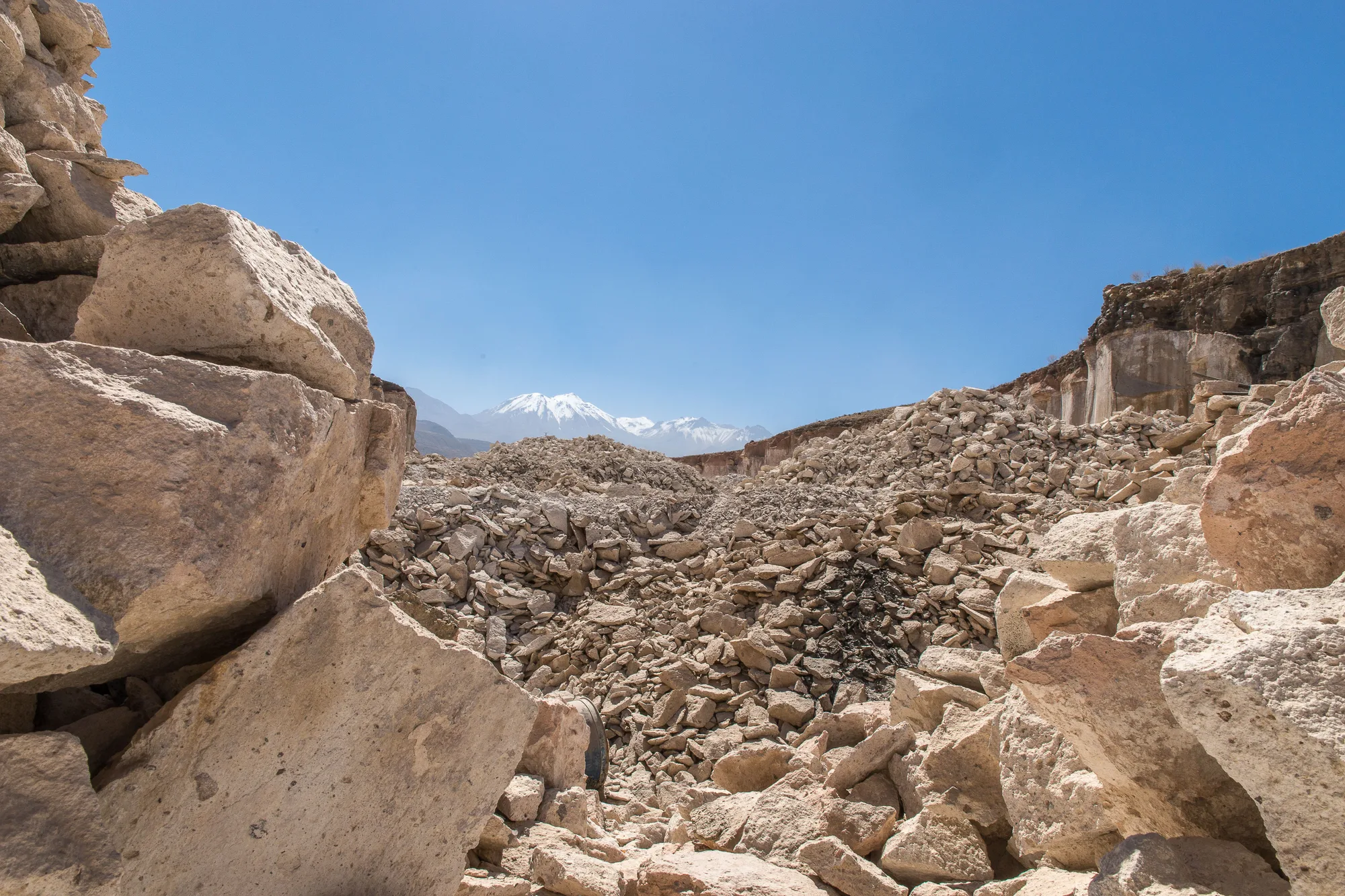 Una cava di roccia con le cime innevate in lontananza, sotto il cielo azzurro