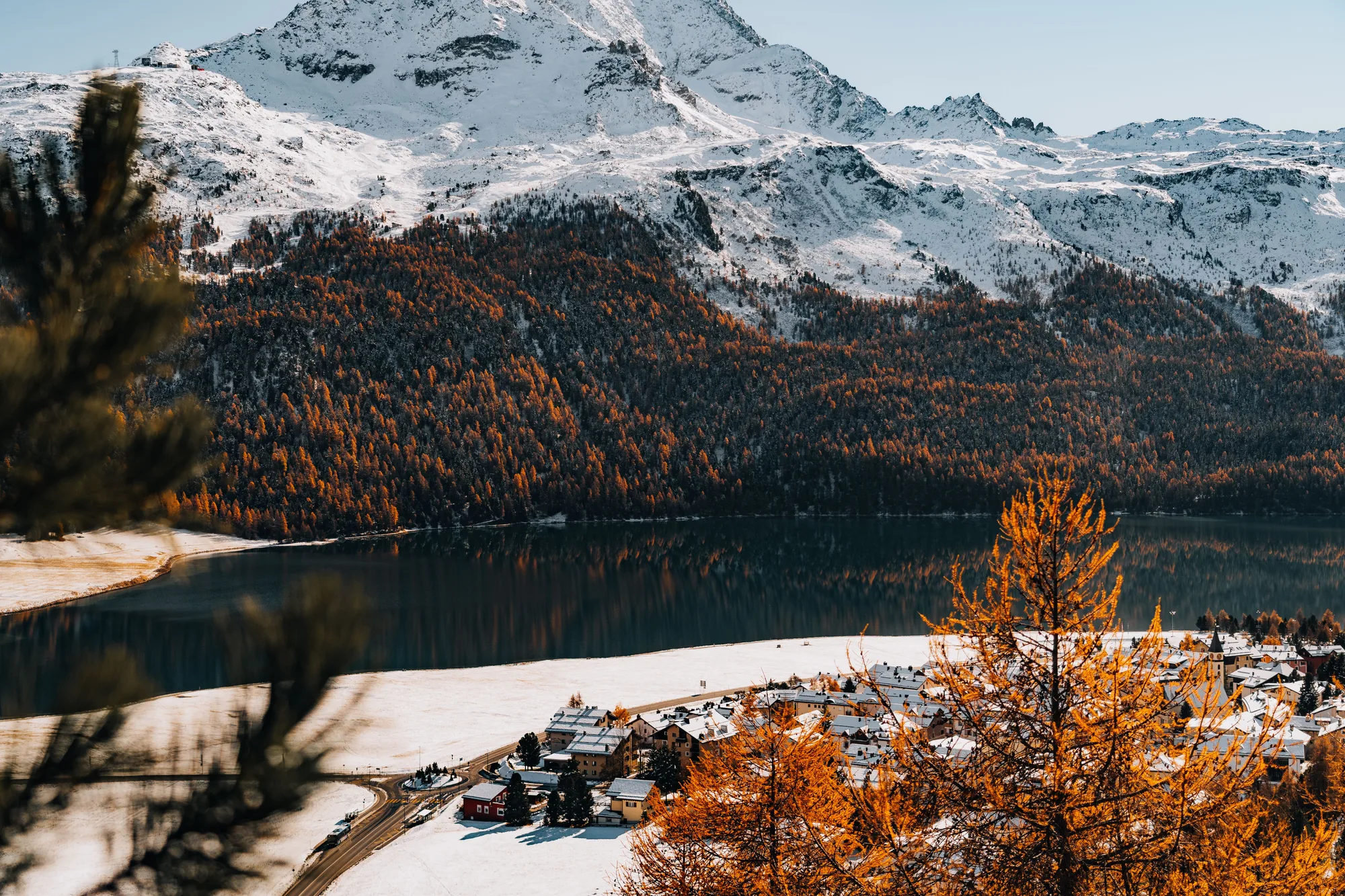 Un paesaggio d'autunno con le montagne innevate, il lago e il paese