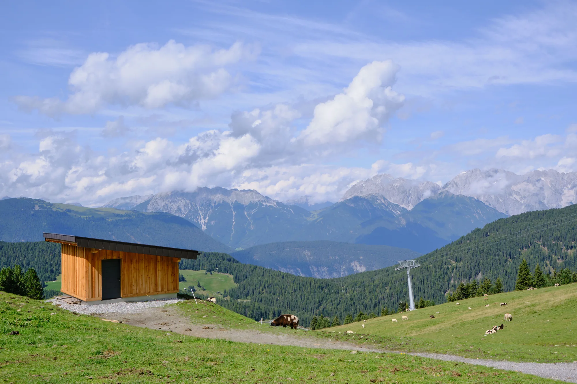 Un fienile di legno fra i prati e le montagne, sotto il cielo sereno