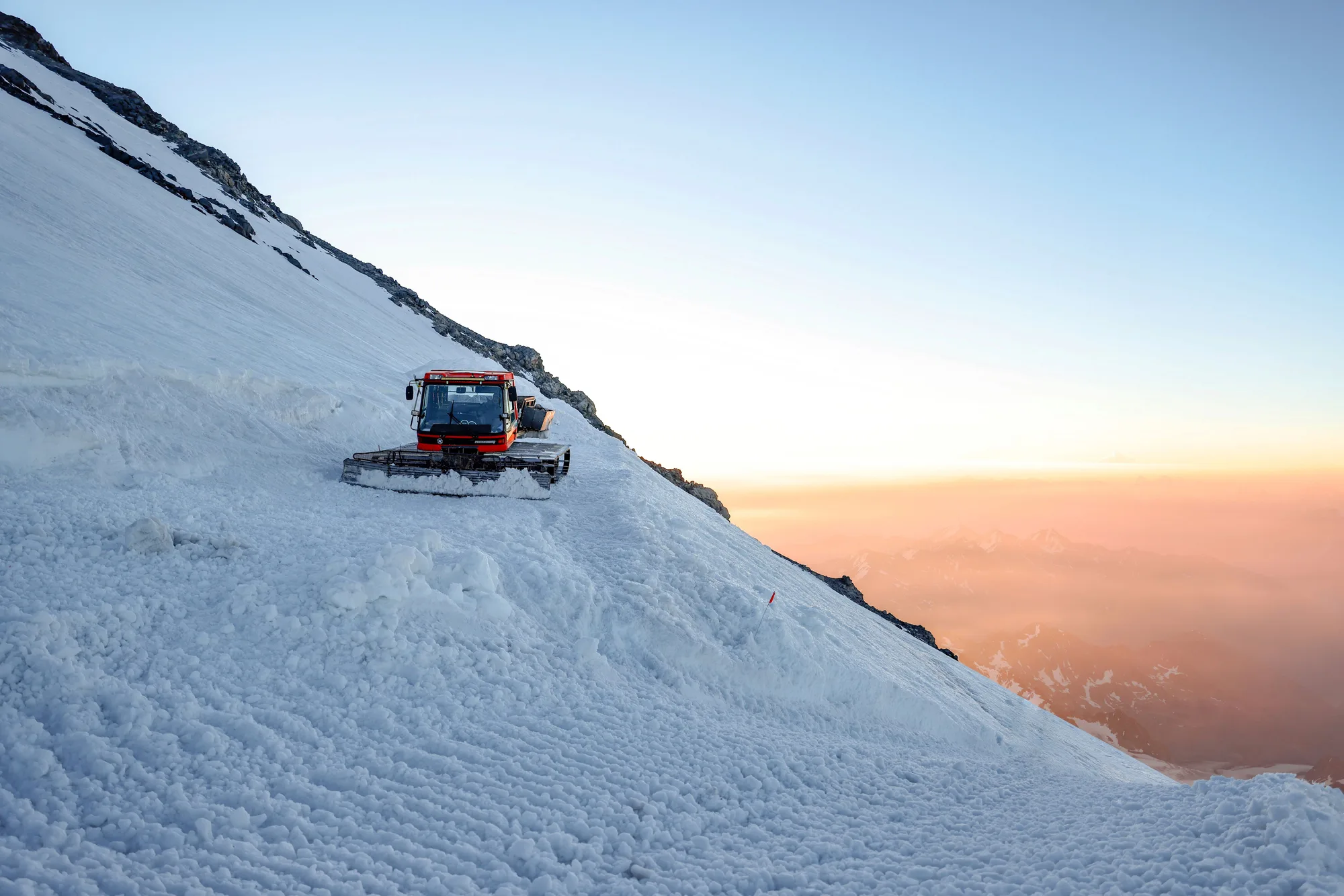 Un gatto delle nevi su un pendio alpino innevato, al tramonto