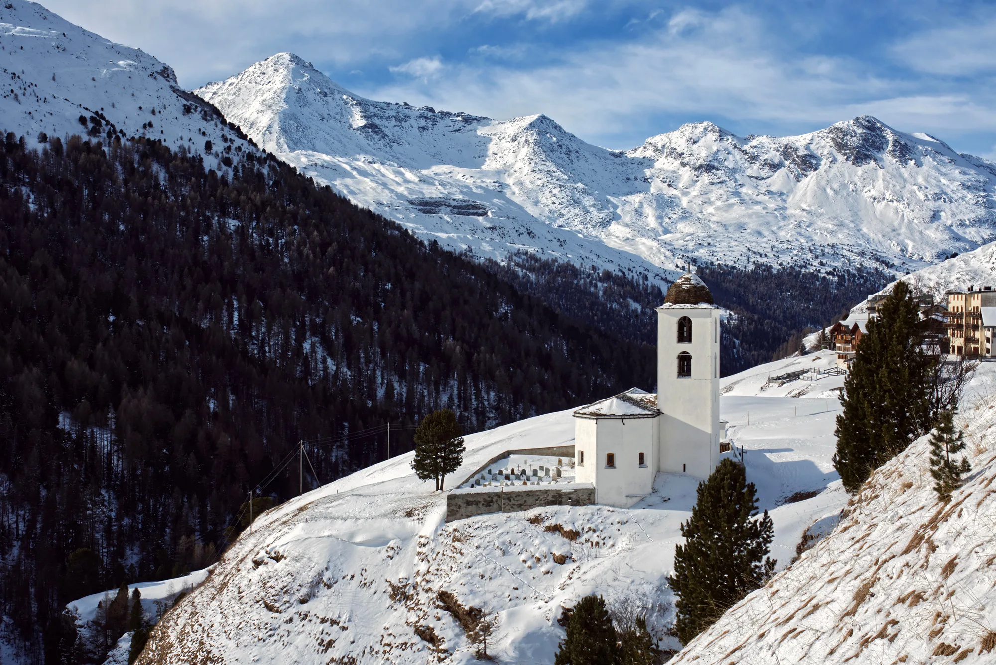 Una cappella di montagna fra le cime innevate e il bosco