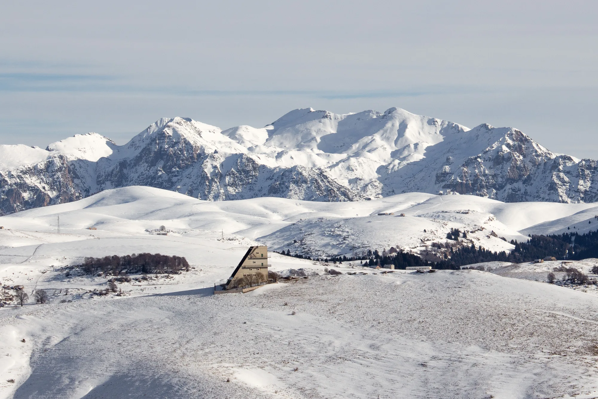 Una catena di montagne innevate con un edificio isolato, d'inverno
