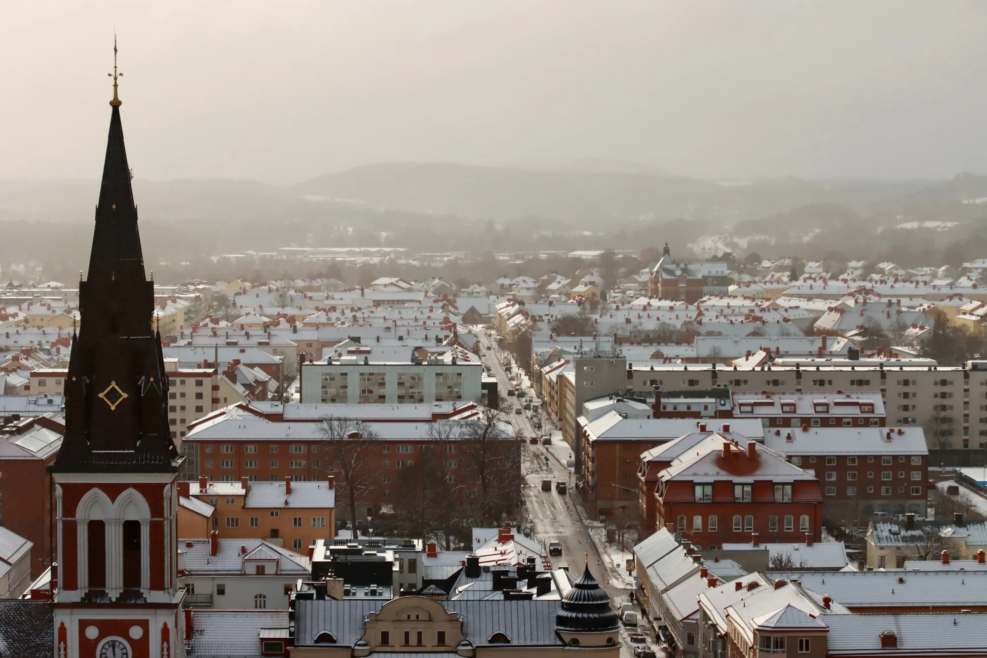 Una città d'inverno con un campanile fra gli edifici innevati, nella nebbia