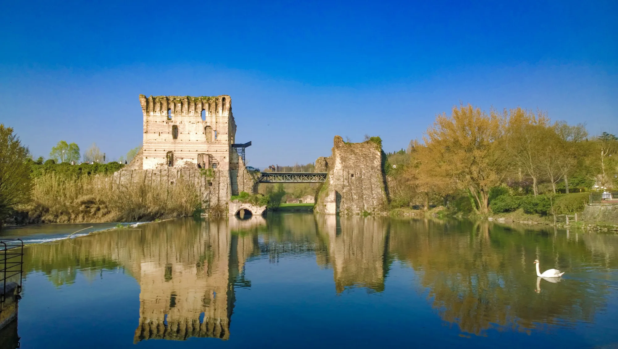 Le rovine di un castello riflesse in un lago calmo, sotto il cielo sereno