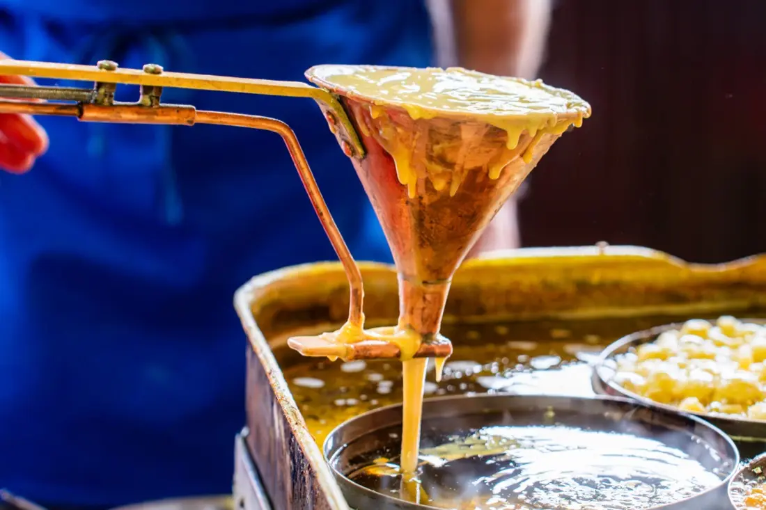 La pastella degli strauben cade dall'imbuto di rame nell'olio bollente